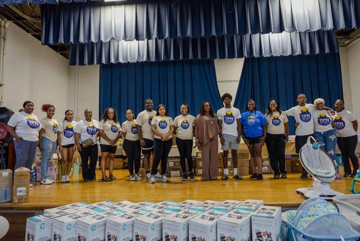 Volunteers on stage behind rows of baby supplies ready for distribution