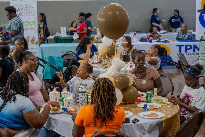 Families sharing a meal at gold and white tables styled for a baby shower